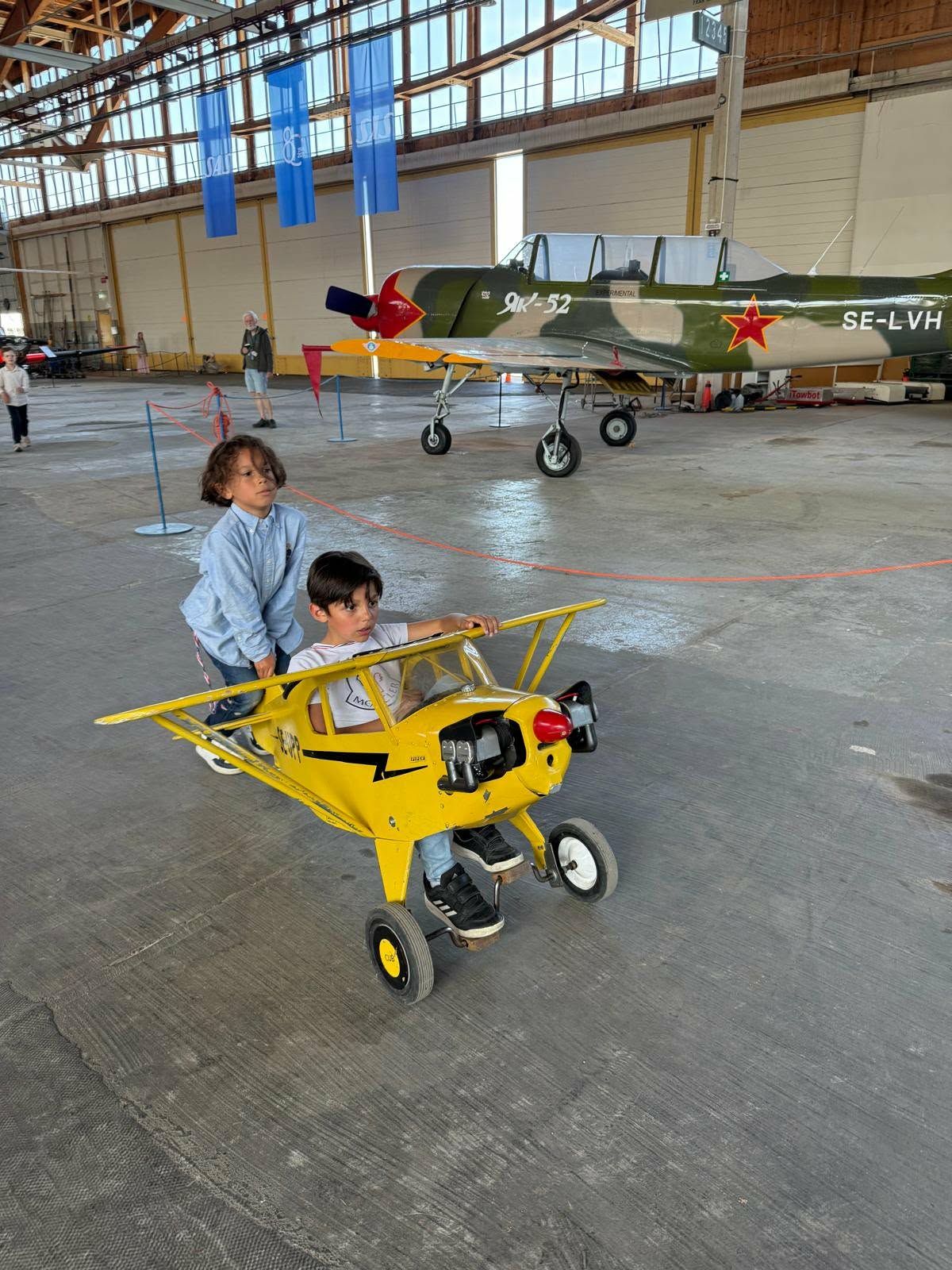 Barn i en miniatyrflygmaskin framför Yak-52 i hangaren