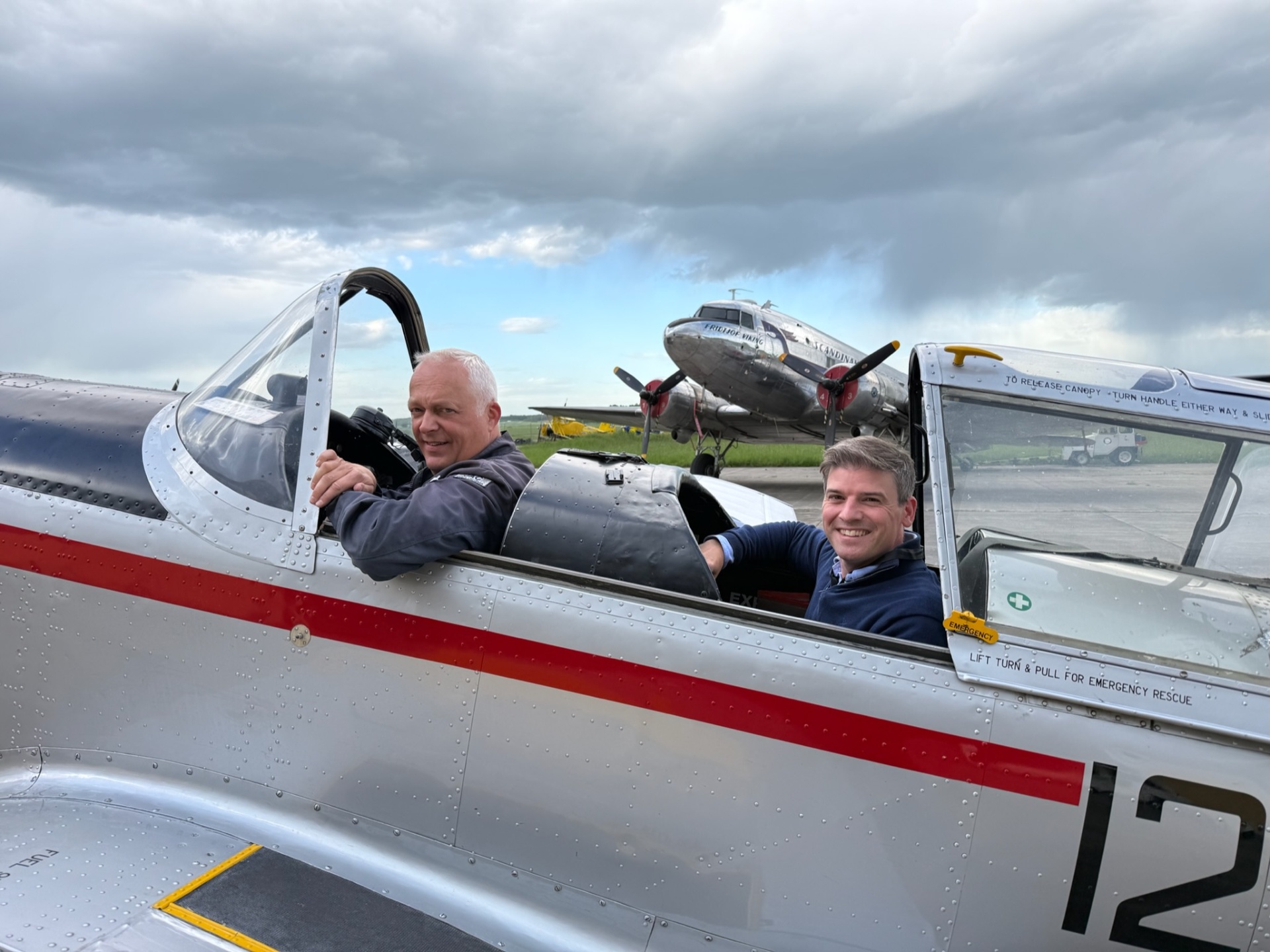 Två piloter i veteranflygplan med DC-3 i bakgrunden